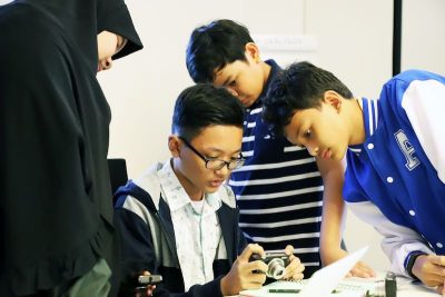 a woman in hijab and three boys review images on digital camera