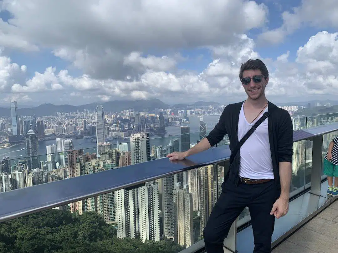 young man in sunglasses poses in front of Hong Kong skyline