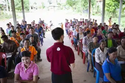 Man wearing Asia Foundation-branded polo speaks to a gathering of people in Laos