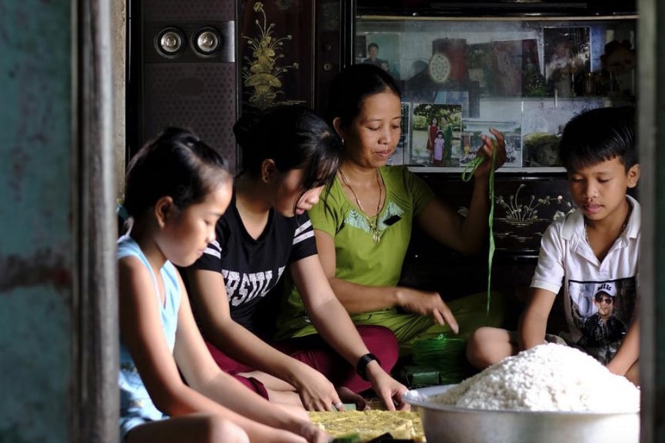 Horizontal photo of a young family sitting on the floor cooking.