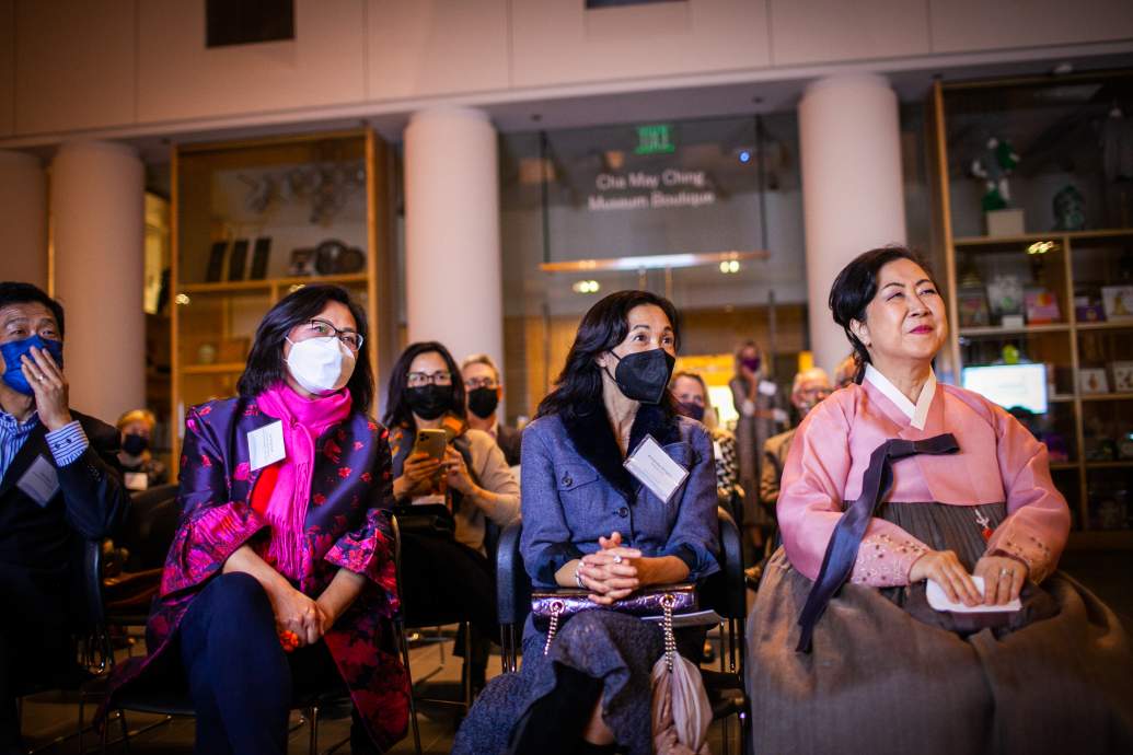 Row of three women and one man in facemasks look off camera
