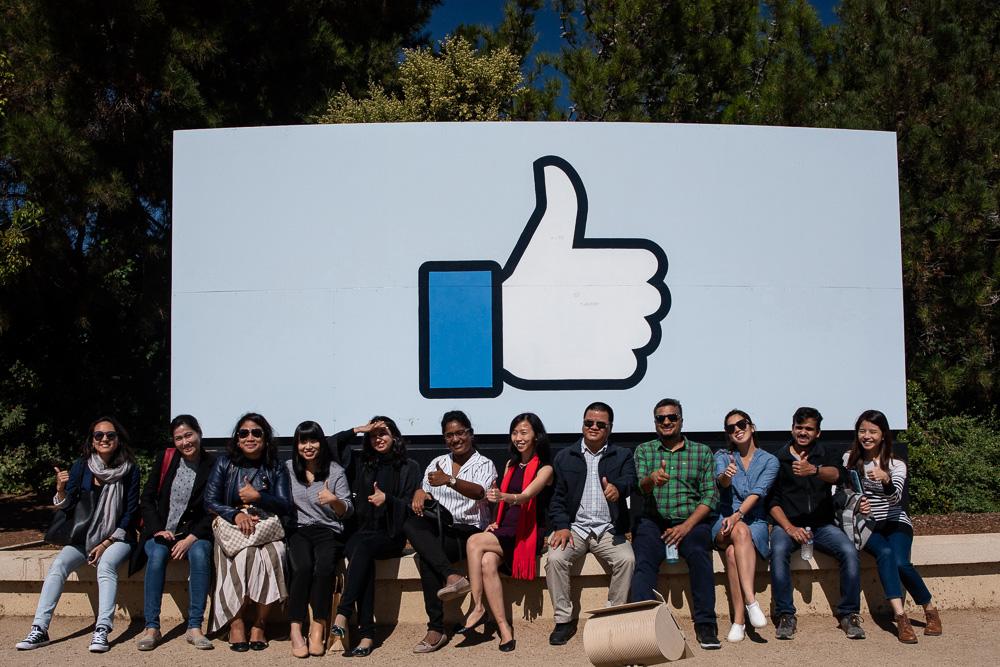 Development Fellows smile for photo in front of Facebook thumbs-up icon while visiting the Menlo Park campus