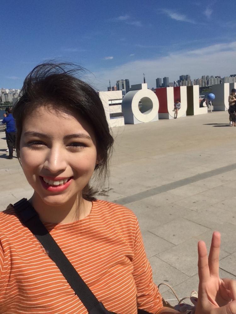 Woman smiles in front of Seoul sign