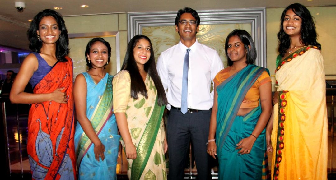 Five young women in traditional Sri Lankan dress and one young man pose and smile at a gathering