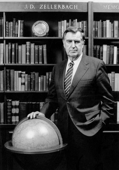 Man in suit stands with globe in front of full bookshelf