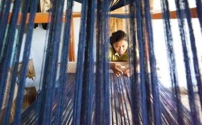 A woman looks closely at strings on a loom