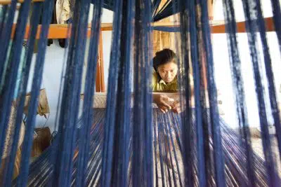 A woman looks closely at strings on a loom