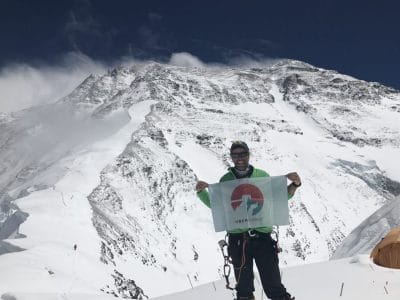 Smiling man in front of mountain holds up "Uber Everest" flag