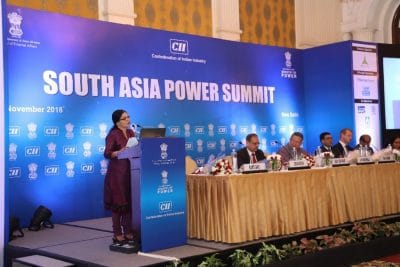 A woman speaks at a podium, while a panel of others look on.