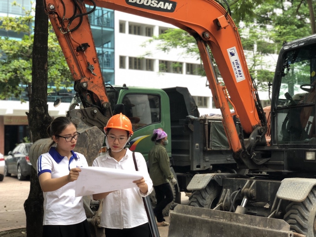 Two young women check blueprints in front of construction equipment
