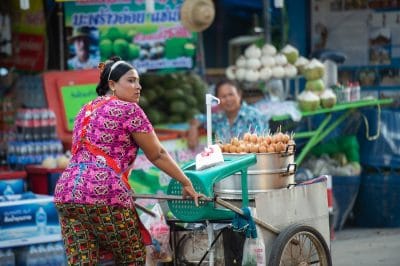 Woman in apron pushes handcart with food on sticks