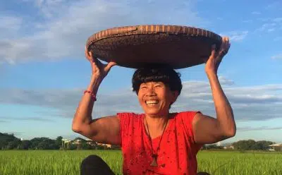 Woman in a red shirt sits in a rice field with a basket on her head