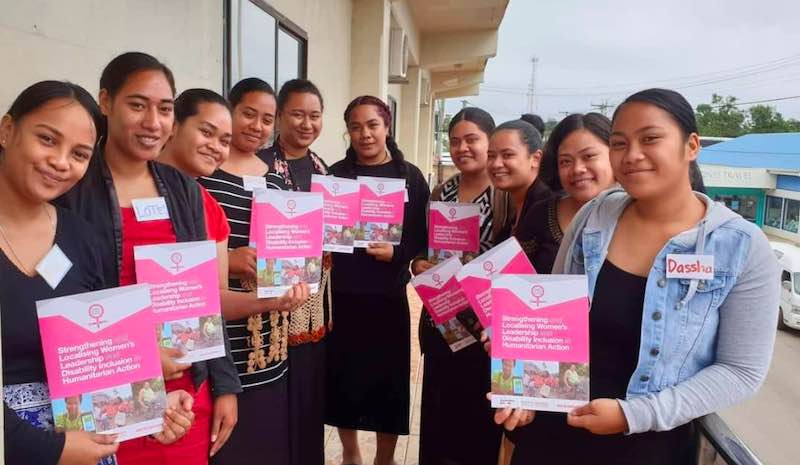 Group of young women pose with brochures detailing women's leadership and disability inclusion in humanitarian action
