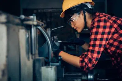 A woman works to fix a piece of machinery.