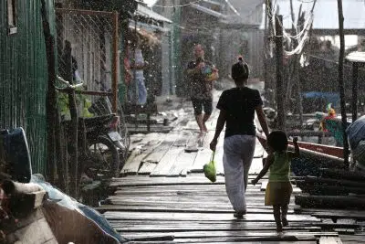 A woman walks with her young child along deck in the rain