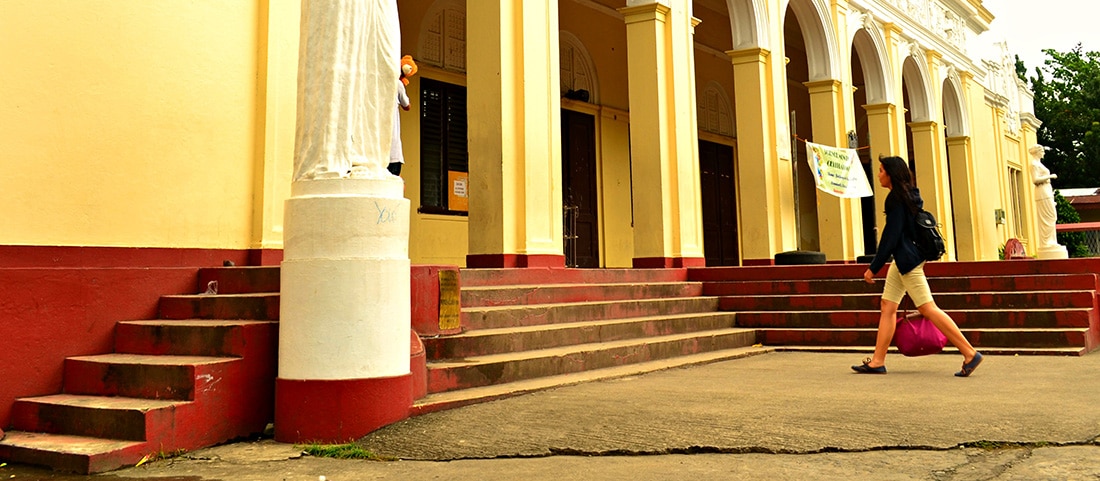 A female student walks into the entrance of a yellow and white school building.