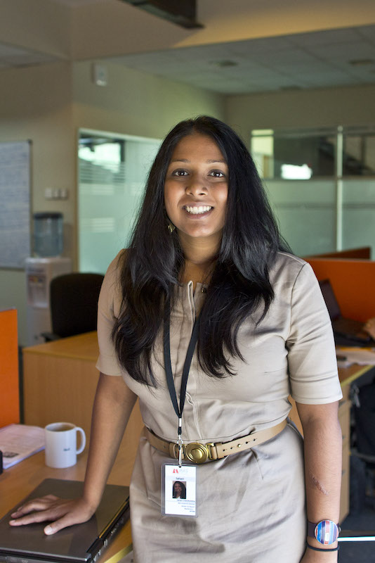 Young woman poses at desk in busy office