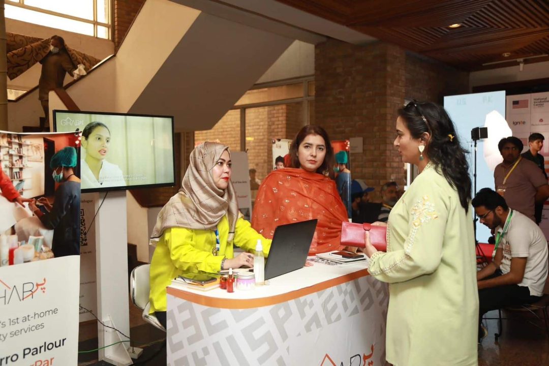 Three women gathered around a booth discuss the product
