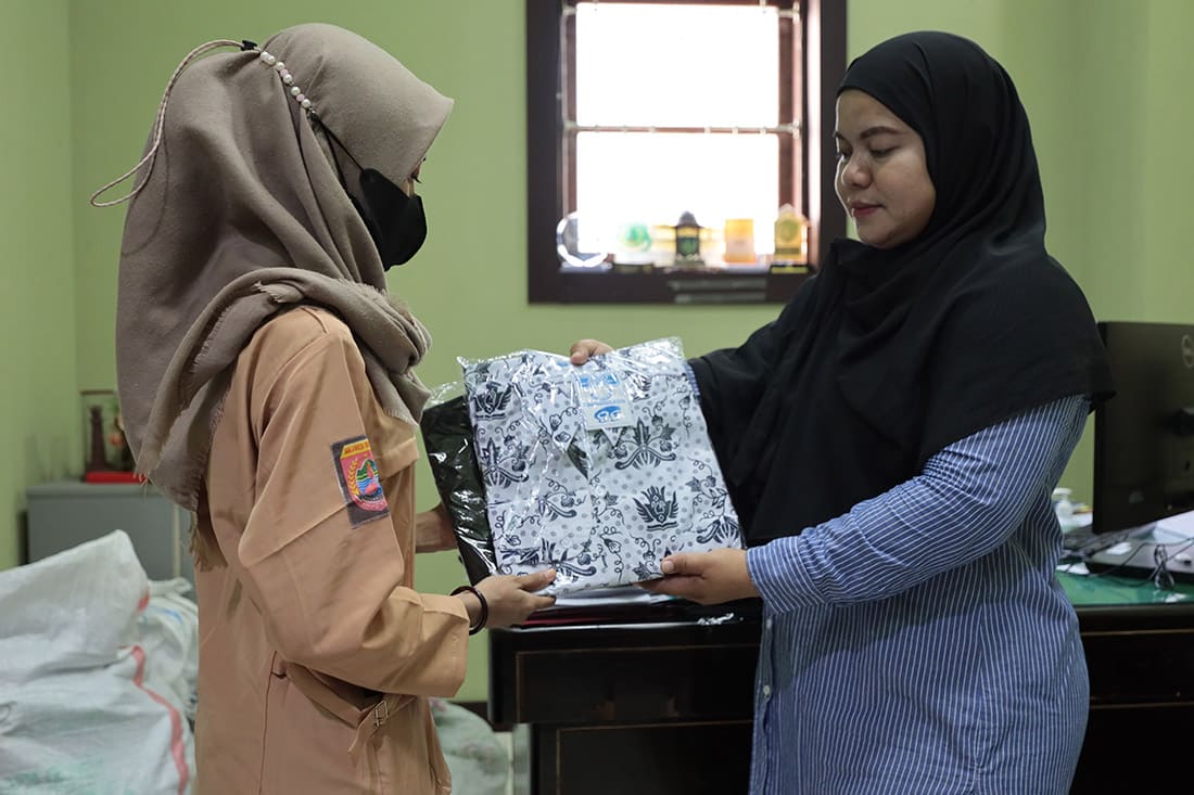 Two young girls stand together. One girls receives a new school uniform.