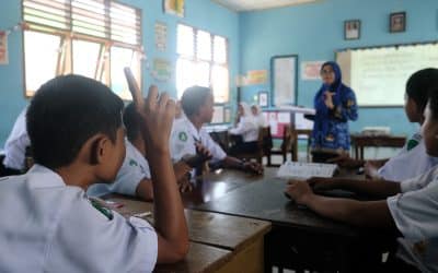 A boy in a school uniform raises his hand in a classroom.