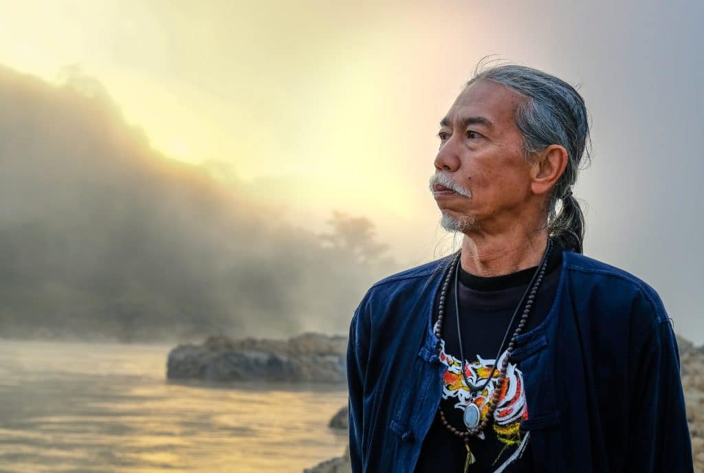 Thai man with pony tail gazes into the distance across a river