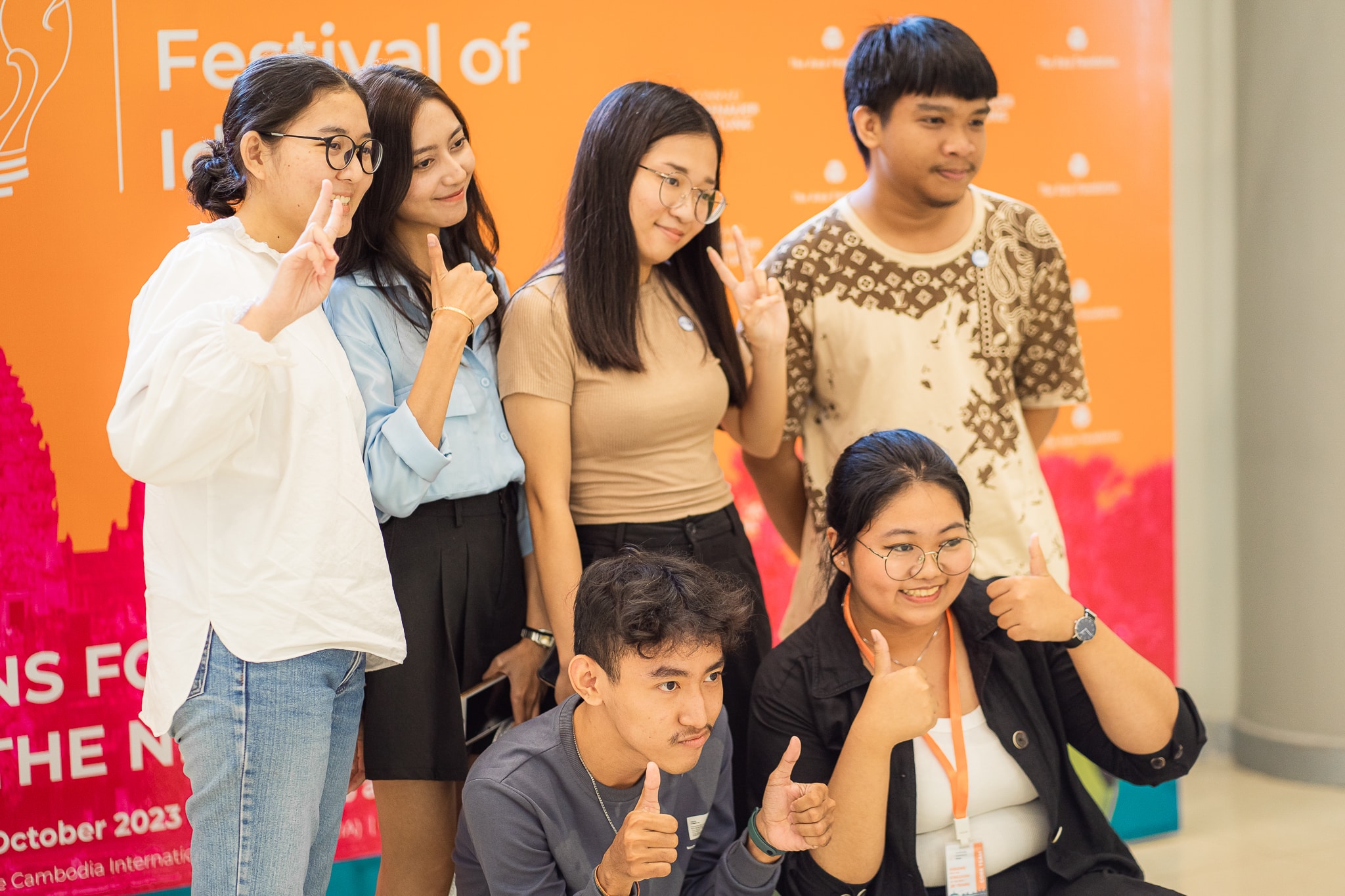 A group of six men and women pose for a picture with peace signs and thumbs up.