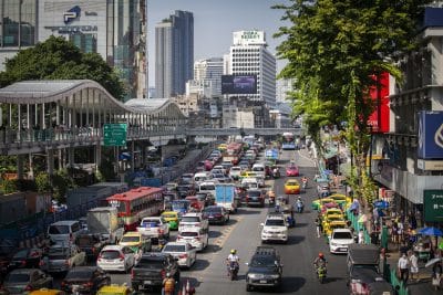Cars stopped in traffic beside bridge with Bangkok cityscape in the back ground.