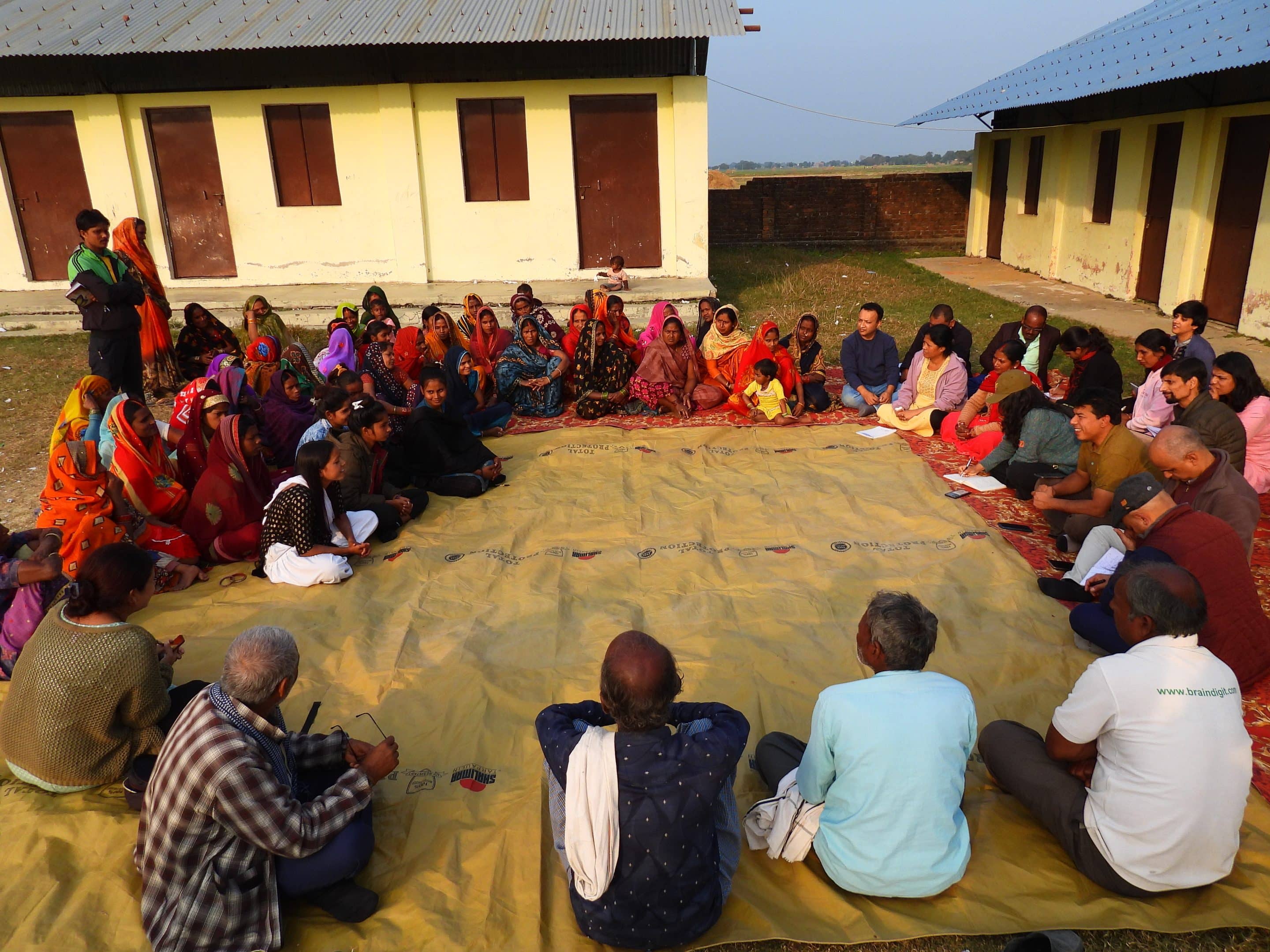 Journalists and members of marginalized communities in Nepal's Lumbini province sit in a circle outside and aside community homes. 