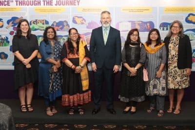 A group of six representatives from the Foundation and regional SAGP CSO partners from the WAVE Foundation in Bangladesh gather next to the U.S. Embassy in Colombo Chargé d'Affaires, Douglas Sonnek. They are posing for a photo with a step and repeat behind them that includes several different initiatives.
