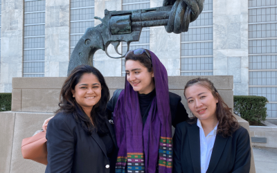 3 women stand in front of a statue of a gun wrapped in a knot.