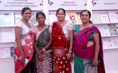 Four women wearing traditional clothing smile for a photo in front of an exhibition.