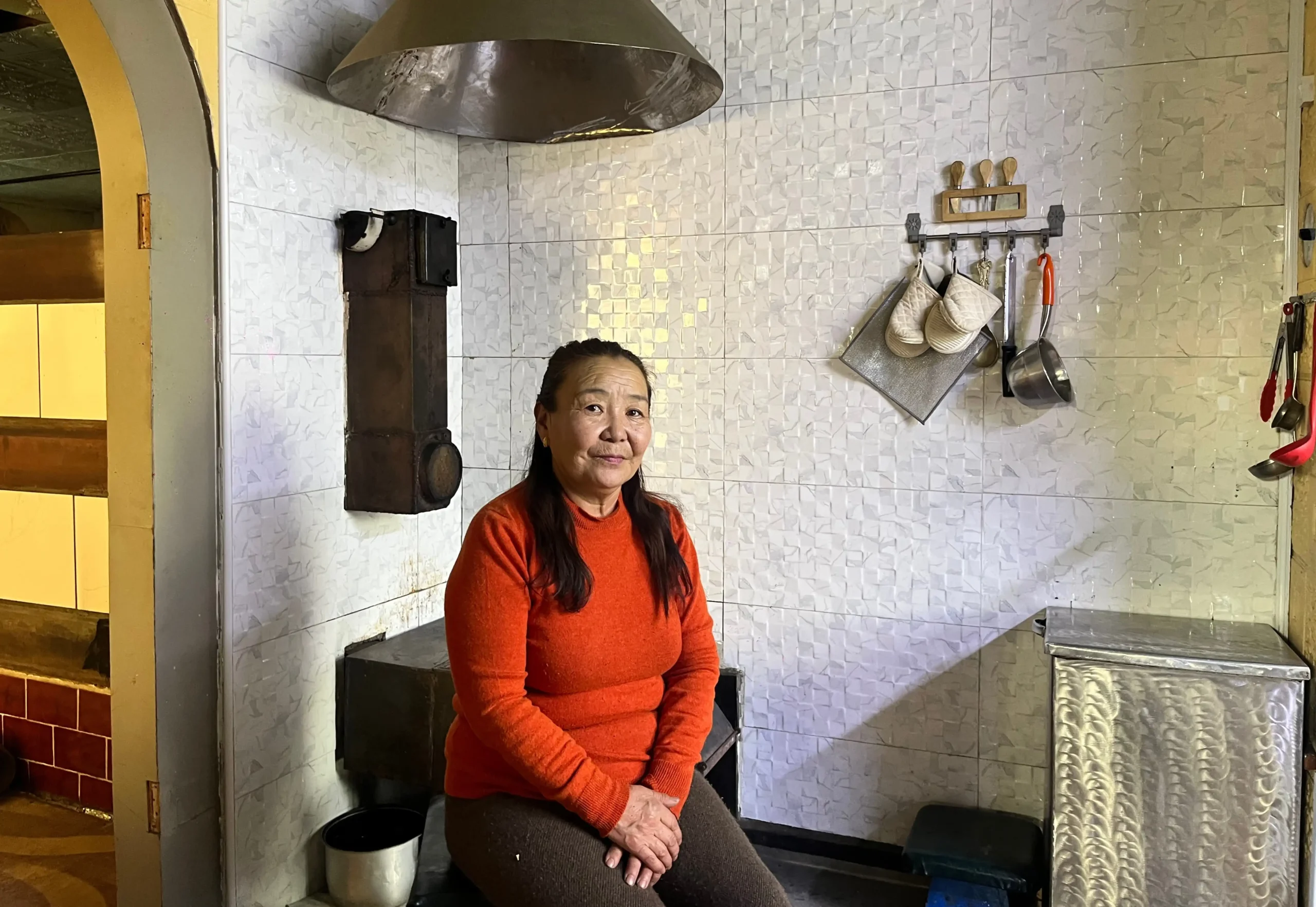 Ms. Davaakhuu sitting in front of masonry stove, November 2025